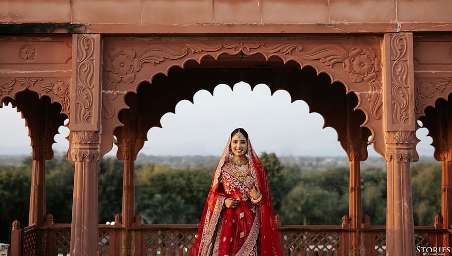 Bride standing under a traditional sandstone arch with scenic backdrop.