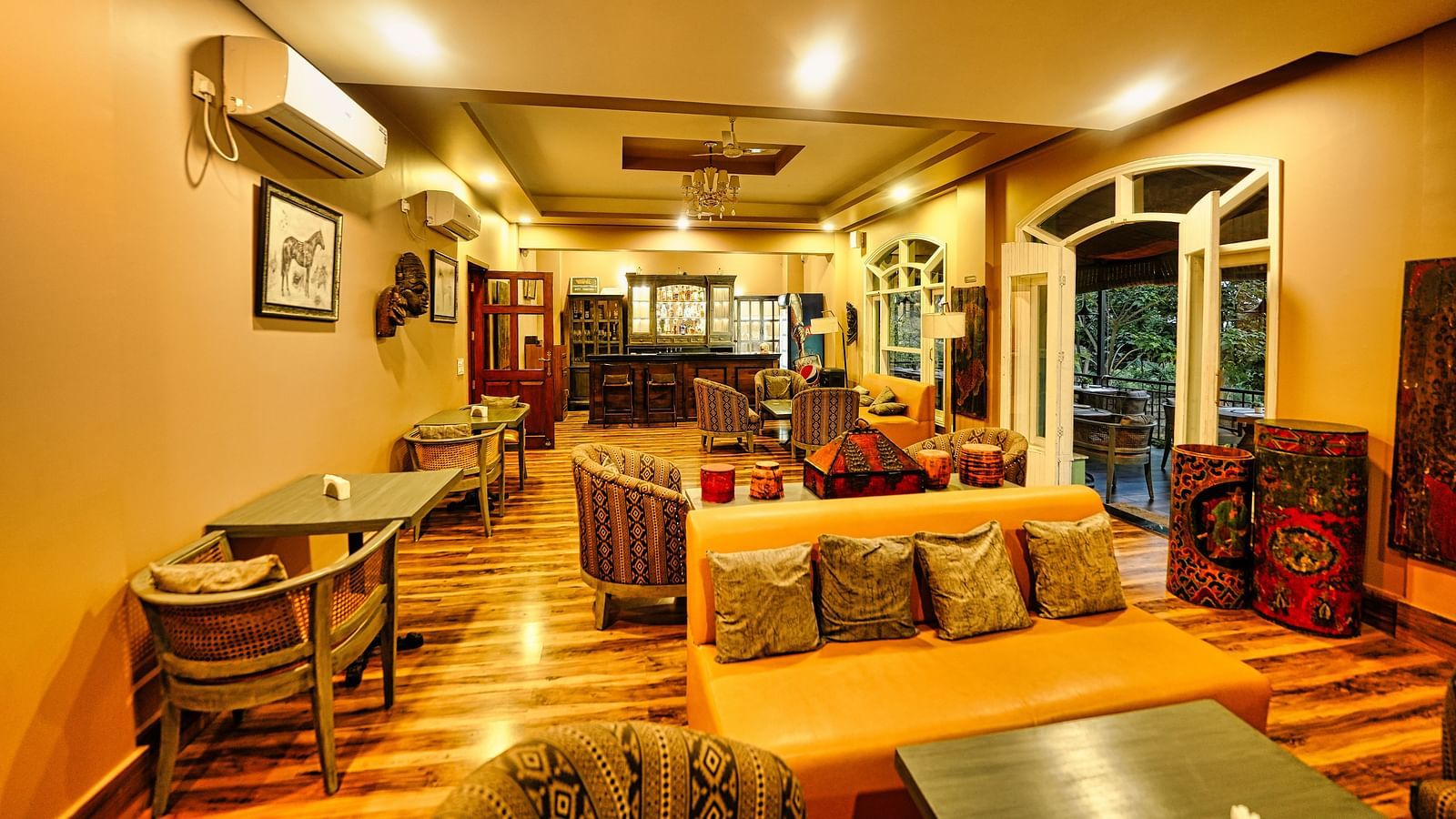 An image of interiors, wooden flooring and brightly lit. with a few sofas, tables with chairs.