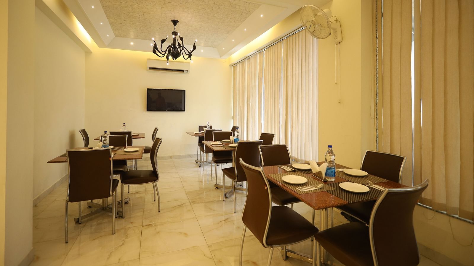 A well-lit dining space with several tables and chairs is decorated with sheer curtains and a chandelier - Asian Suites Cyber Park, Gurgaon