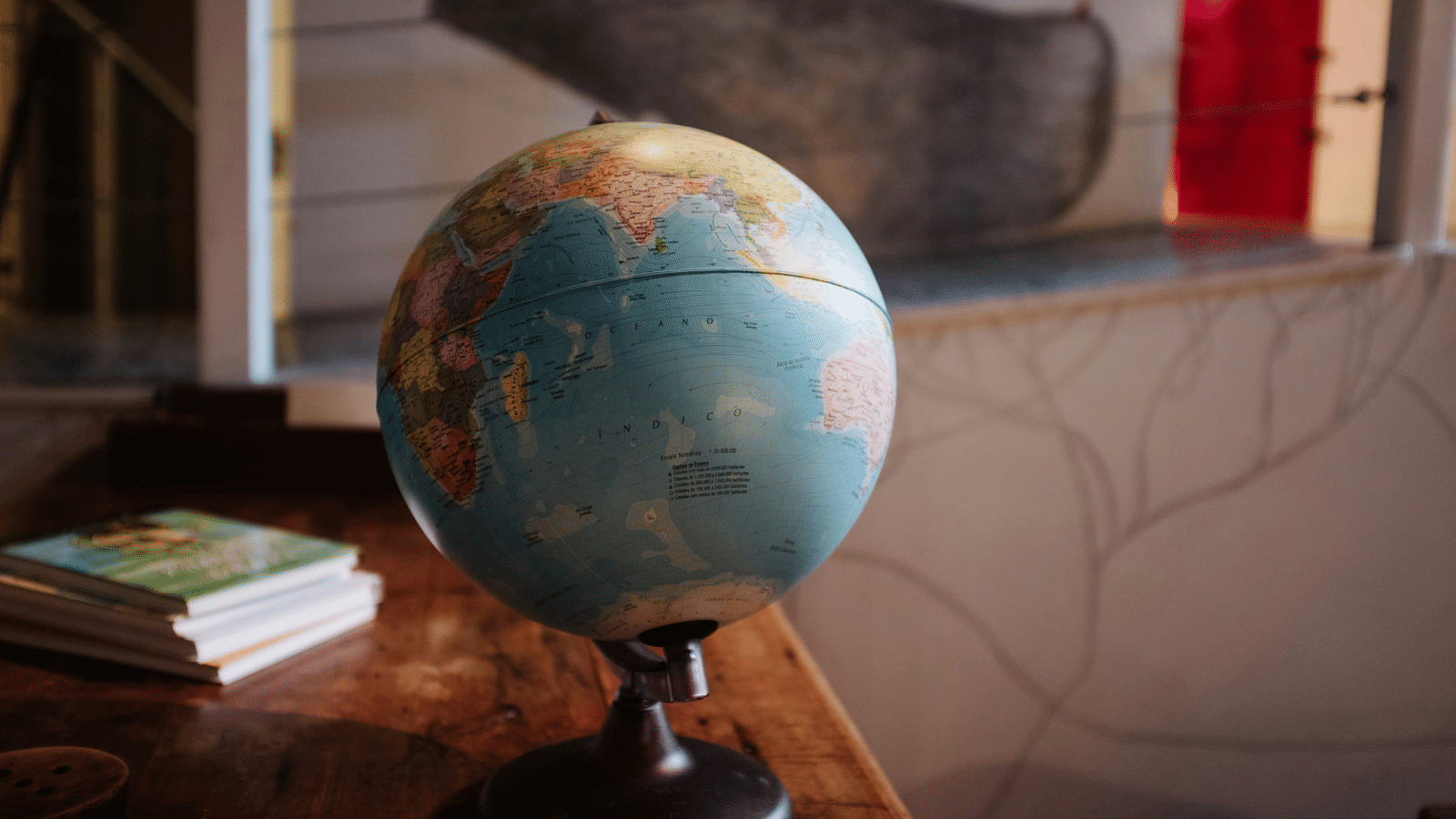 A globe kept on a table with books behind it.