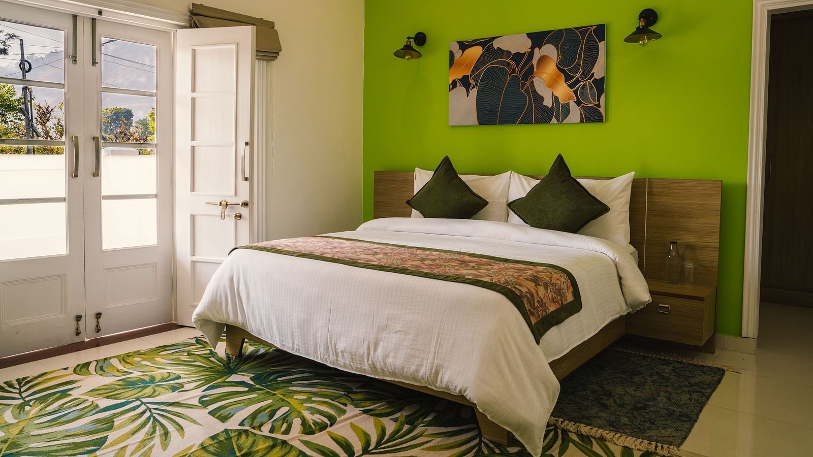 A spacious room at BluSalzz Villas - The Green Roof, Bhimtal featuring a large bed, a photo frame above the headboard, a carpet, and a door leading to the balcony.