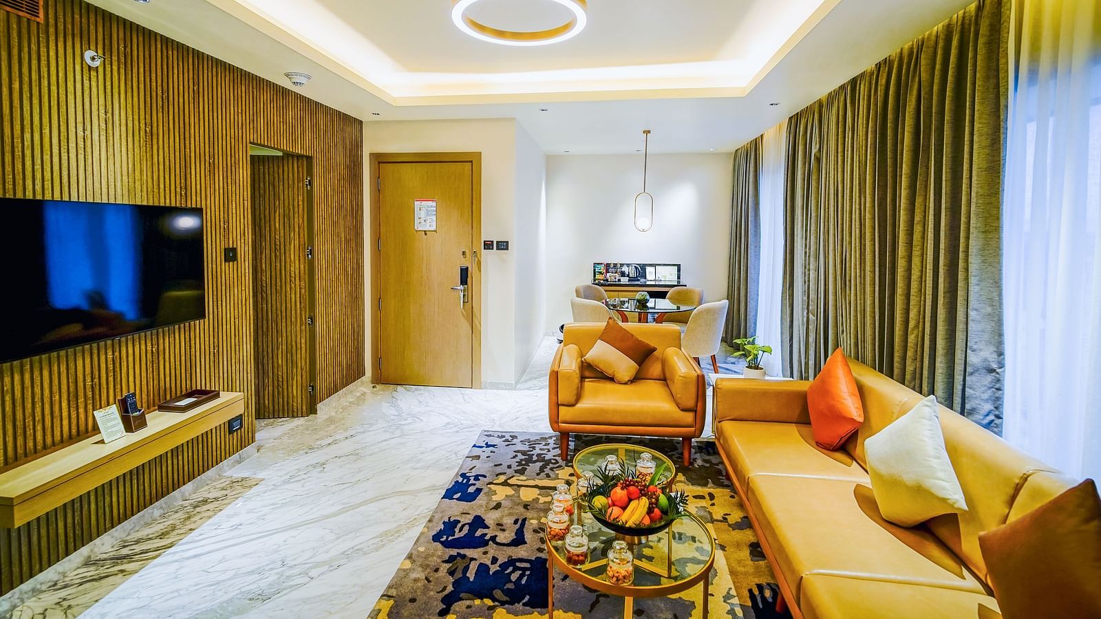 A living room in suite in Madurai filled with amenities like couches, a coffee table, and a wall-mounted televison - Grand Madurai by GRT Hotels