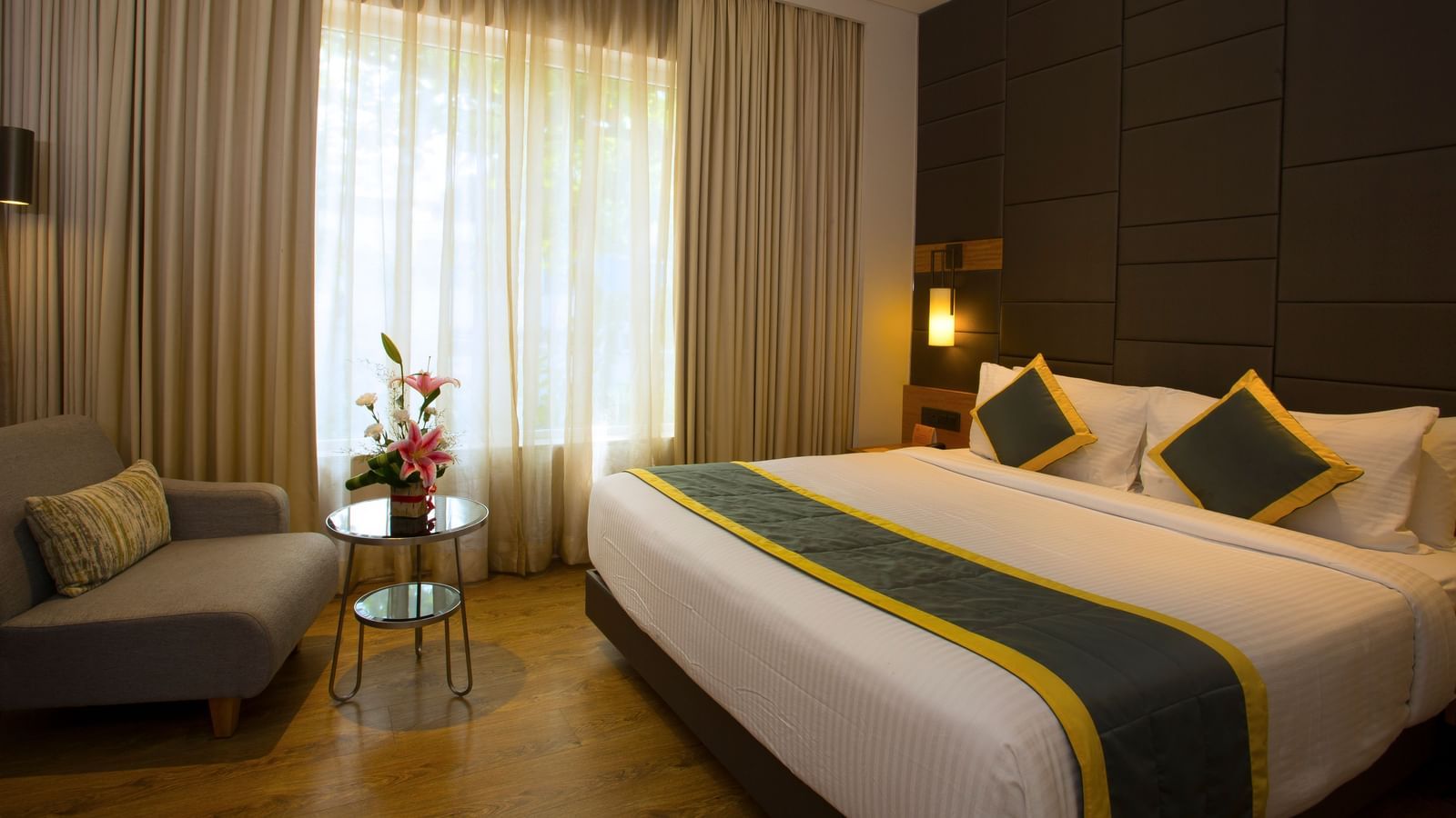 a bedroom with a large bed and a sofa opposite the the bed, with a small table in the middle - Hotel Fountain Tree By TGI - JP Nagar, Bangalore