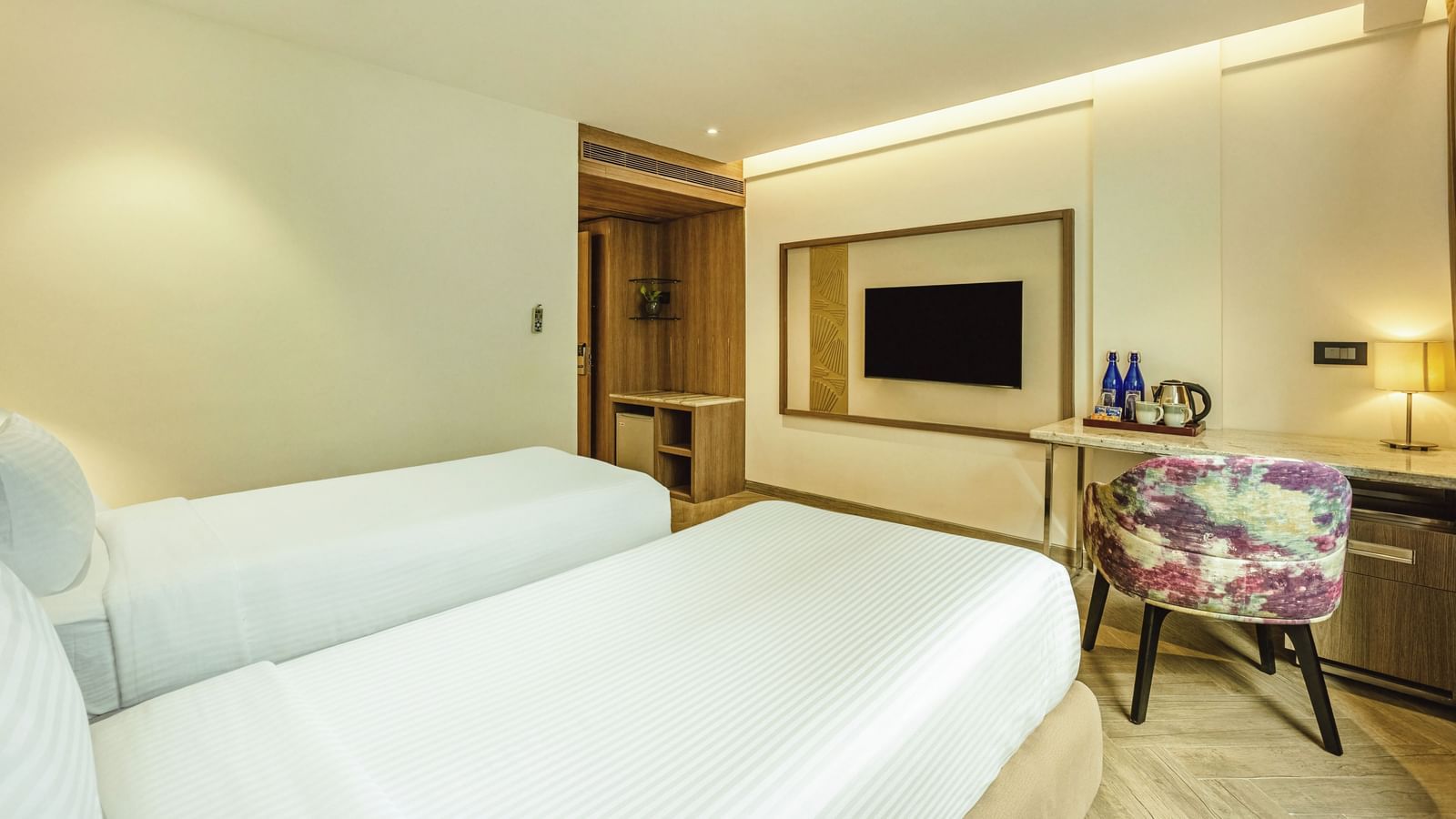 A twin-bedded room with a television and a desk, seen from an angle, at Mango Hill Central, Chennai.