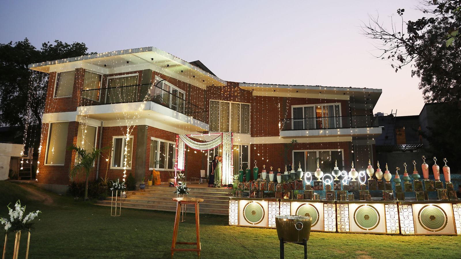 Main building of Tisya Farms, Gurgaon at dusk with lit landscaping and a clear view of the entrance area.
