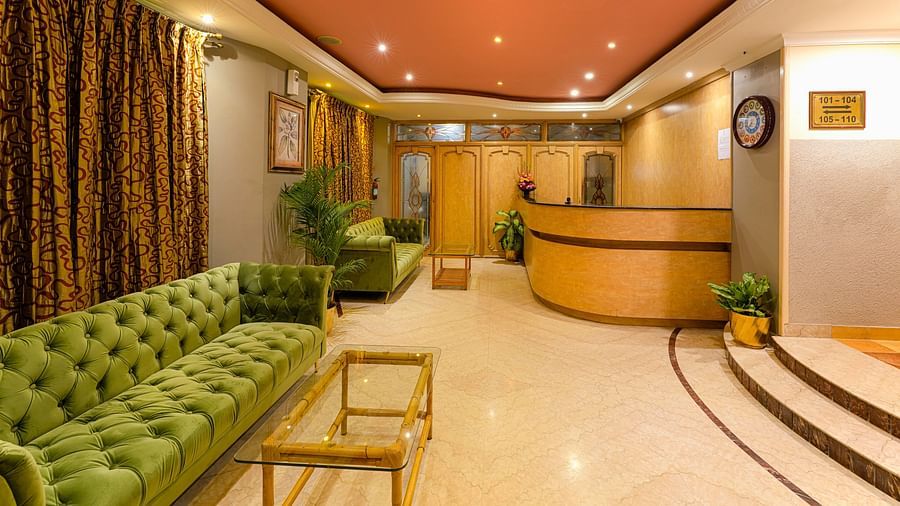 A cosy reception area with green couches and warm lighting - Cross Roads Inn, Bengaluru