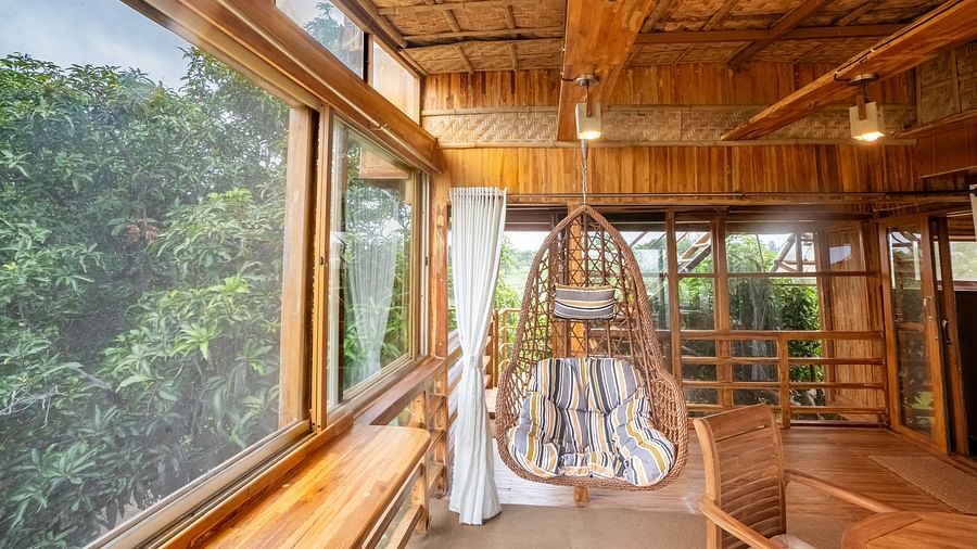 A wooden room with a swing, big window and views of greenery