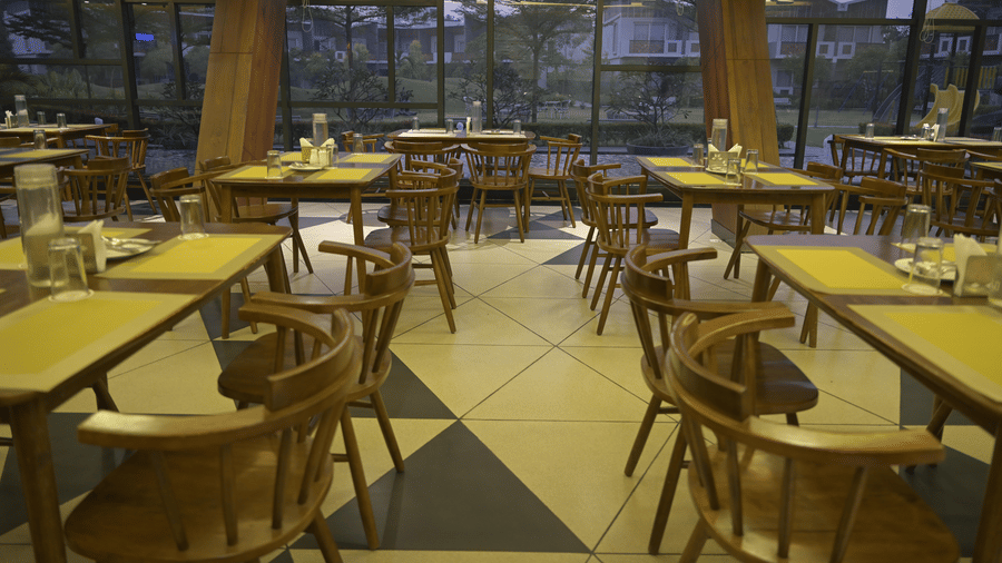 Multiple wooden dining tables and chairs on a geometric tiled floor at Hotel Sonar Bangla, Mayapur.