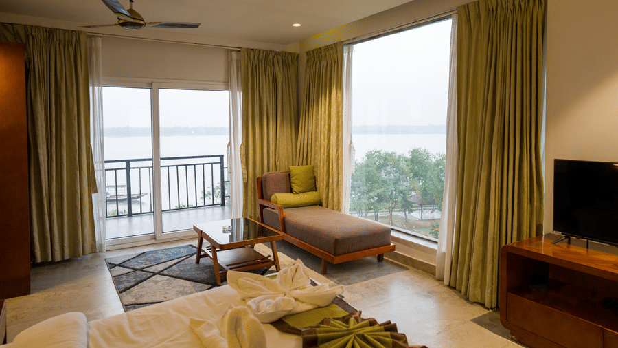 Deluxe Room sitting area with green curtains and balcony access at Hotel Sonar Bangla, Taki.