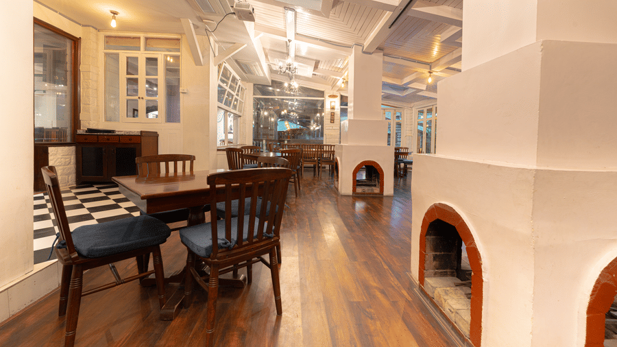 A charming indoor bistro setup with white-painted brick walls, checker board accents, and a fireplace - Johnson Lodge & Spa, Manali