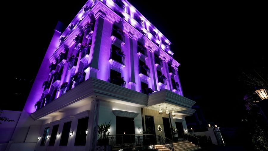 Facade of M2 Square by Monday Premium during the night with violet exterior lights illuminating the entire building.