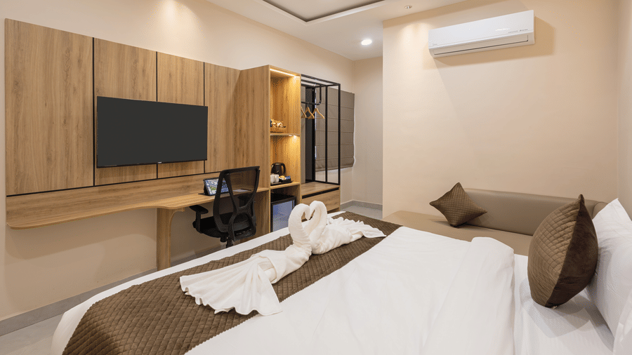 A bedroom showing a king size bed with towel art, a wall-mounted TV unit, and an office desk with a chair at Monday Hotels & Suites Madhapur Hyderabad.