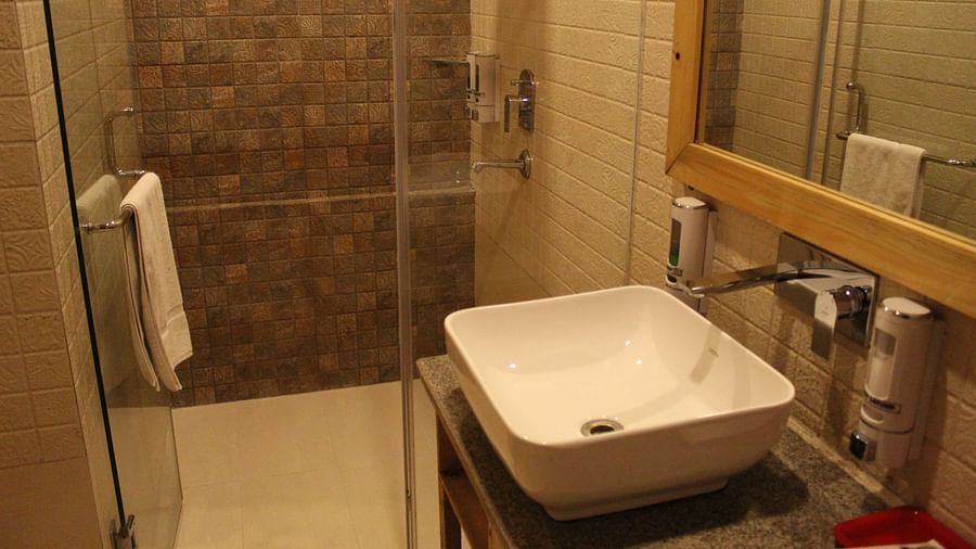 Modern bathroom with a glass shower, white sink, and large mirror at Dagshai Manor Kasauli - Inde Hotels.