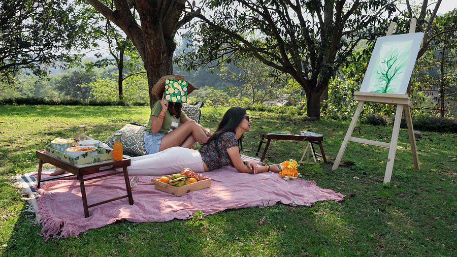 Two people laying on a picnic mat with a snacks table and watching the canvas in a grassfield at the Sylvan Retreat, Dehradun.