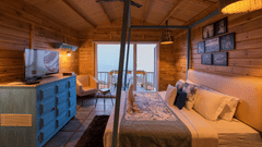 A bedroom at Polo Cherrapunjee Resort with a bed, a colourful dresser, seating area, and glass doors opening to a balcony with scenic views.