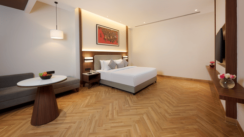 Skywings Sarovar Portico Mathura suite room with king bed, herringbone wood flooring, work desk, framed wall art, and bright natural lighting.