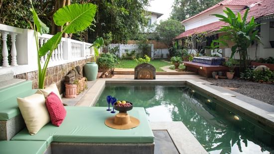 An image of a plunge pool with a seating arrangments on the side of the pool surrounded by trees and plants at Lamrin Ucassaim Hotel, Goa