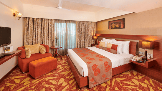 Room at Pride Premier Nagpur featuring a plush bed with lamps on the both sides on nightstands and a TV mounted in front o the bed
