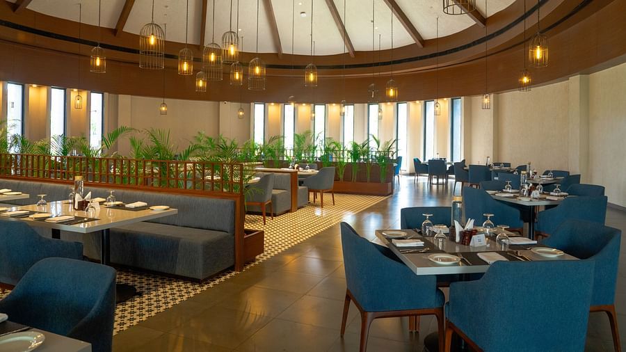 A spacious, elegant dining area with teal chairs, round tables, and a high domed ceiling with natural light at Ananta Spa and Resort, Ajabgarh.