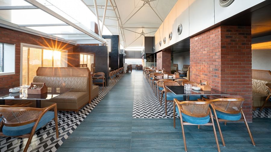 A restaurant interior with a long dining area lined with tables and chairs. The floor is tiled in a black and white geometric pattern - Clarks Inn, Indore