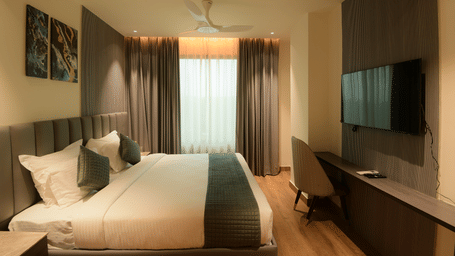 A king size bed facing a wall mounted television, a desk, and curtains at Awesome Palace, Guwahati Airport.