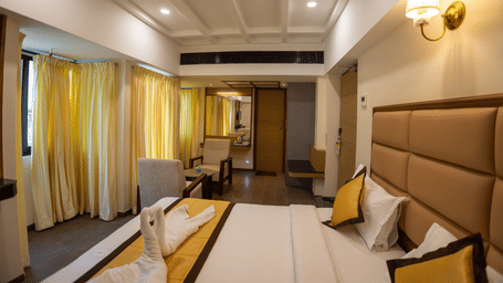 Executive Premium Room interior displaying the bed setup, wall lighting, window curtains, and hallway entrance at Hotel Grand Sabarees Madurai.