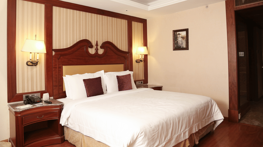 Spacious king bedroom with wooden flooring, warm lighting, and elegant interiors for comfortable day stays near Chennai airport | Hablis Hotel Chennai