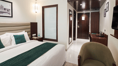 An image of a hotel room with a large bed, a green chair and a wall-mounted television - Deventure Sarovar Portico, Patel Nagar
