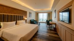 An image of our premium room in Ajmer featuring warm lighting, a king size bed, cosy furniture, a television and views of the city - Sarovar Portico, Ajmer