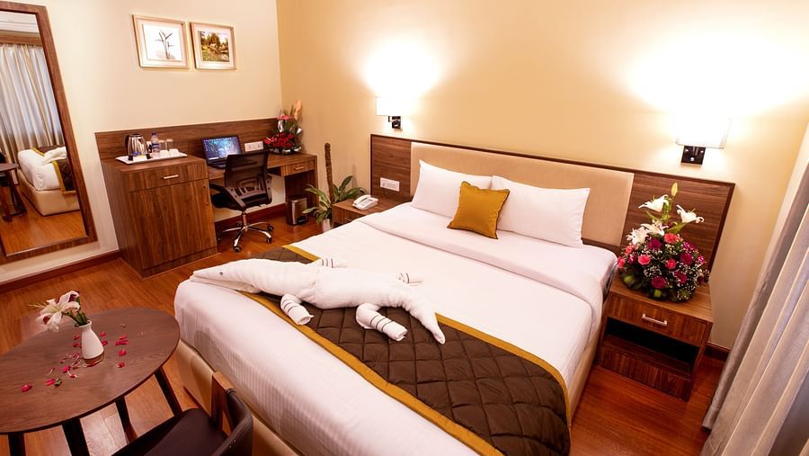 A warm and inviting hotel room with a plush bed, wooden furnishings, a work desk, and soft lighting for a cosy ambiance. - RK Gardenia, Surya City