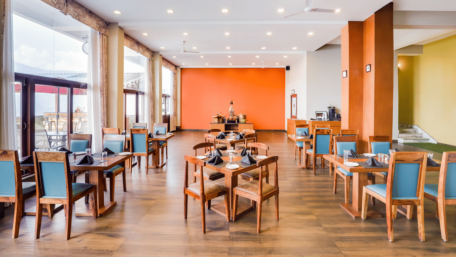 Bright and spacious dining area with wooden furniture and orange accent wall at Mount Himalayan Hotel & Spa, Gangtok.