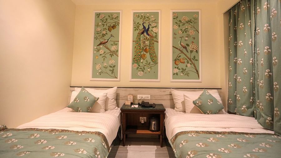 Twin beds placed side by side with a wooden bedside table in the middle, and there are three photo frames positioned above the headboard | Panna Vilas Udaipur