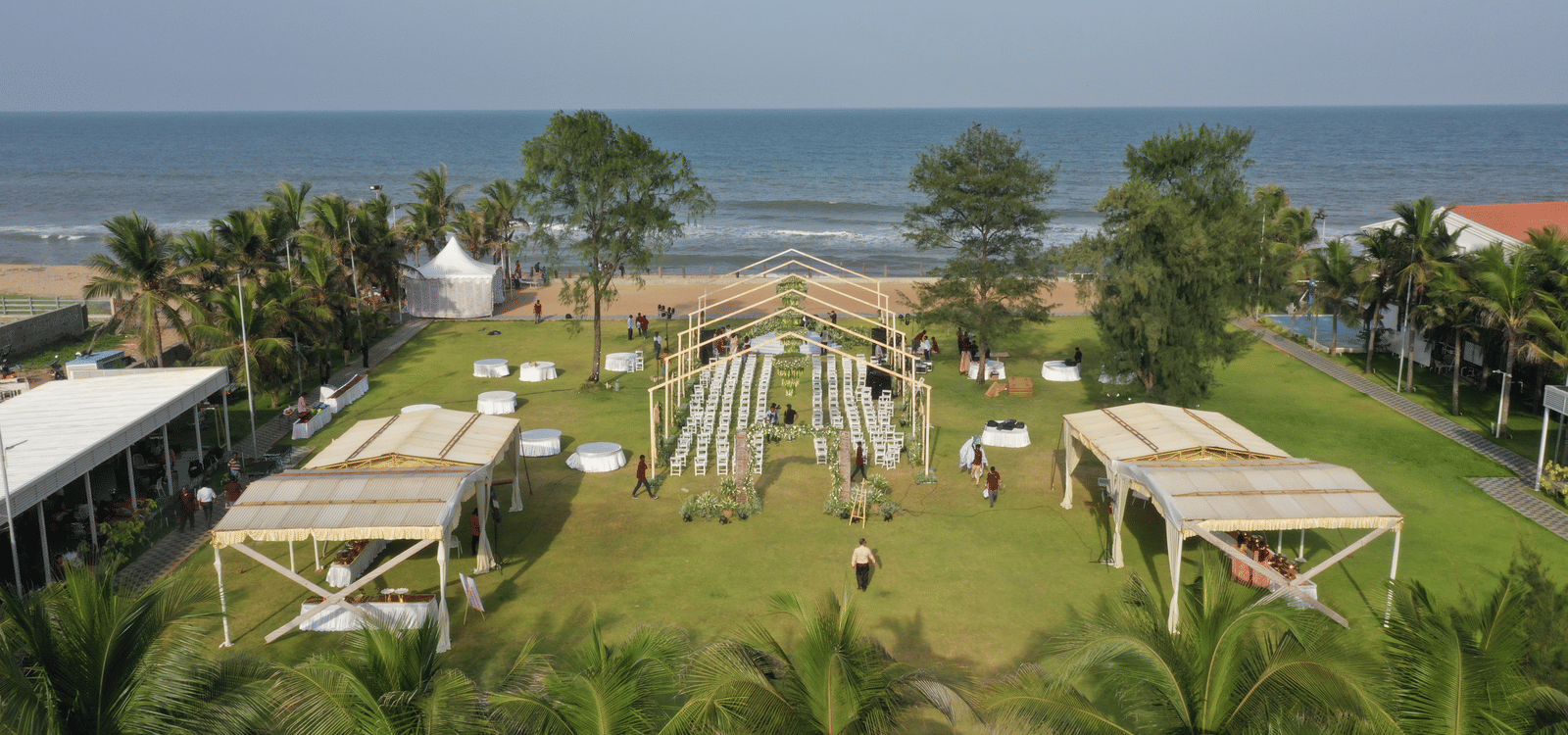 An aerial view of the lawn set up for a beach-side event, featuring shaded buffet counters, and a sea-facing seating area at Grande Bay Resort & Spa, Mamallapuram.