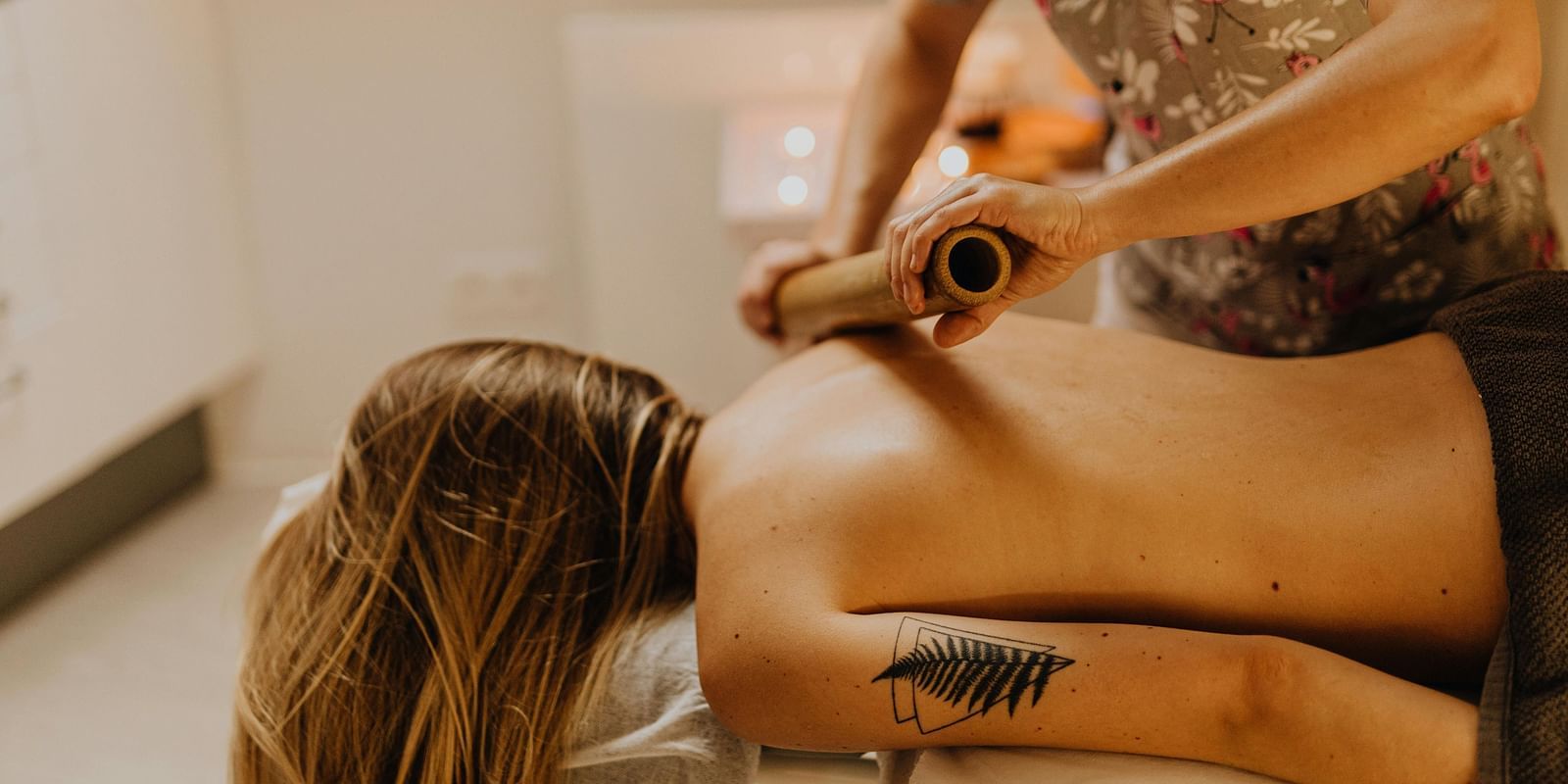 A therapist using a bamboo roller on a woman's shoulder.