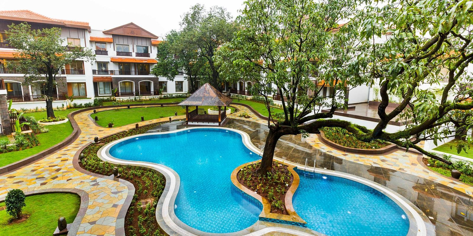 Swimming pool with a tree in the centre of the pool and the resort in the background - Rhythm Lonavala.