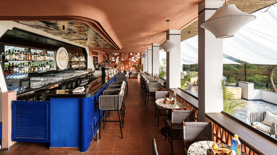 A stylish outdoor bar with an array of beverages, a long counter, and high stools for seating.