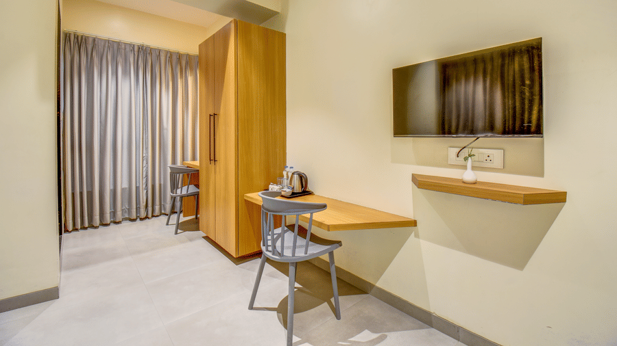 Room with wall-mounted television, writing desk, chair, and window curtains at VITS Select Nashik Hotels & Resorts