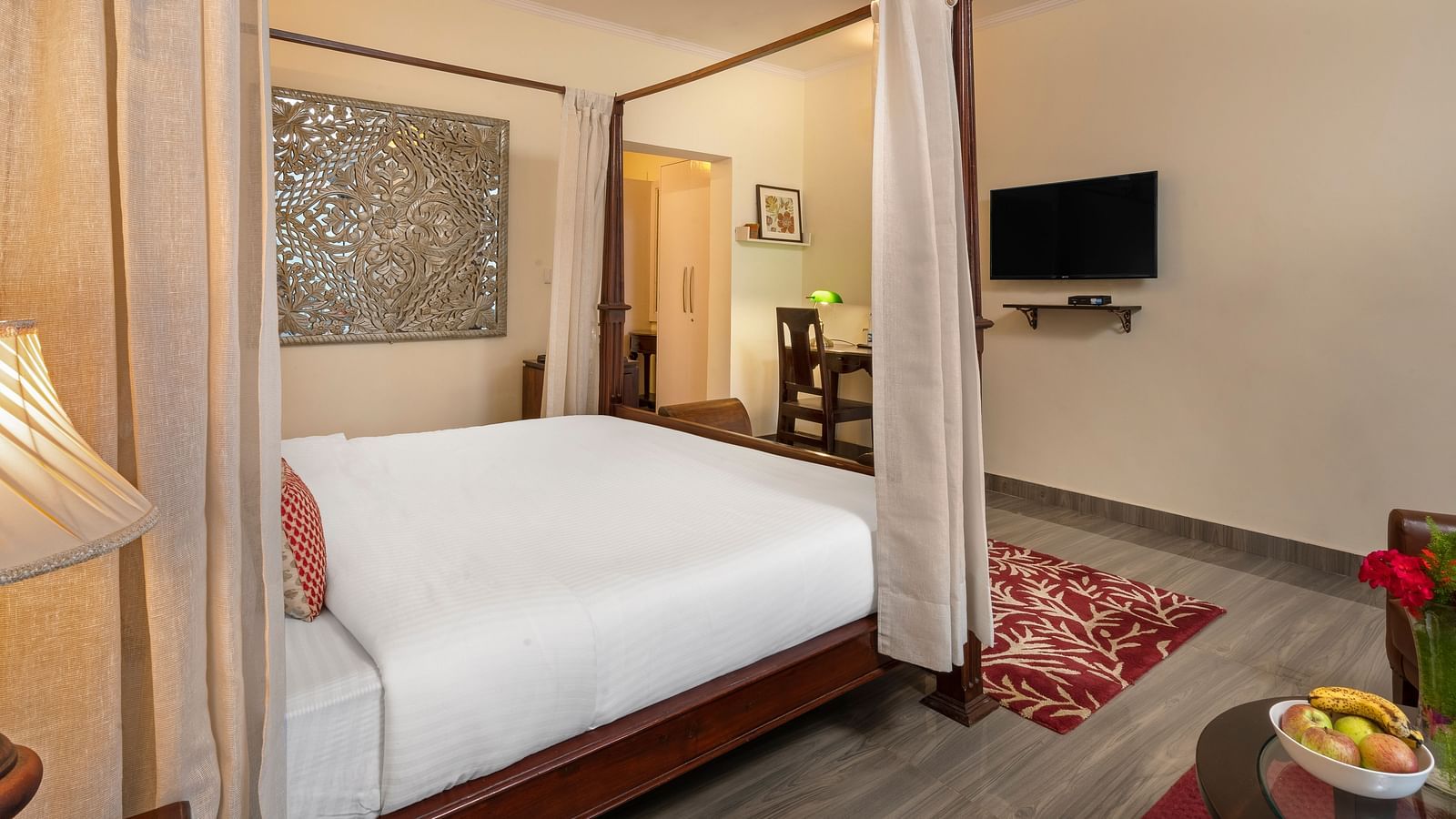 An image of a bedroom with poster beds, a flat TV screen, and a table which has fruits in it  - Suvaasa, Ramgarh