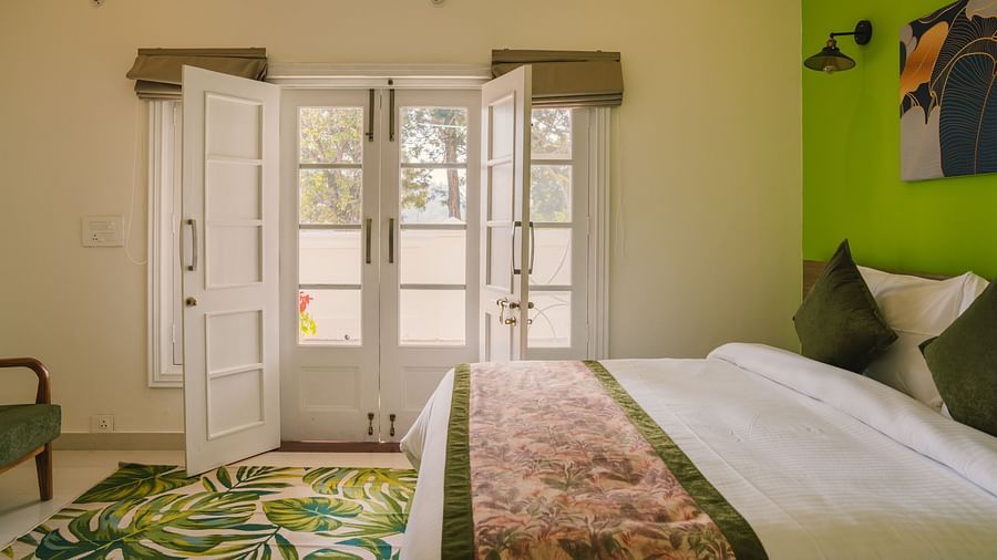 A side view of the neatly made bed with a carpet on the floor and a pair of glass-panel doors leading to the balcony at  BluSalzz Villas - The Green Roof, Bhimtal.