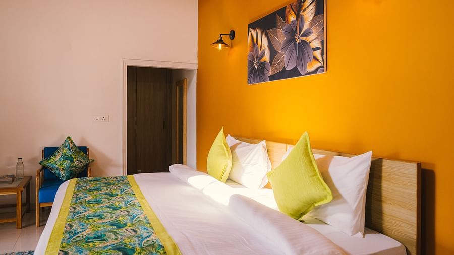 A side view of a neatly made bed with a photo frame above the headboard, two night lamps on either side, and a door in the background at BluSalzz Villas - The Green Roof, Bhimtal.