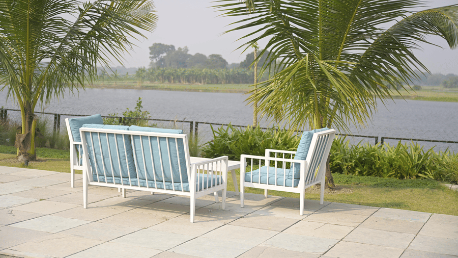 Outdoor seating by the river with palm trees and a peaceful water view at Hotel Sonar Bangla, Mayapur.