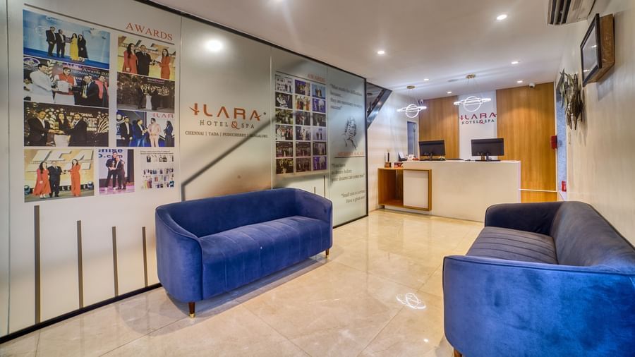 Part of the hotel lobby with two comfortable blue sofas and a minimalist reception area, leading towards the entrance at Ilara Hotels & Spa, OMR, Chennai.