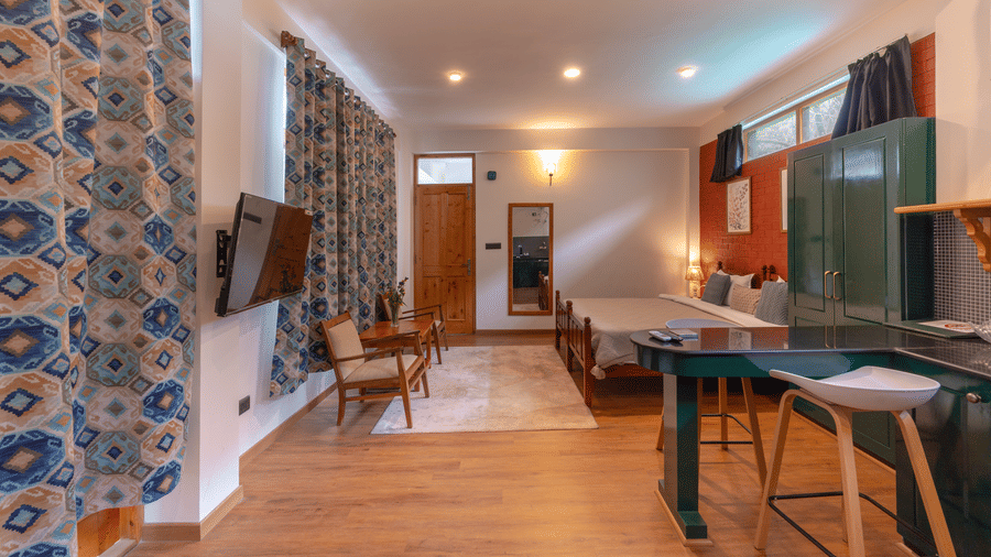 Wide-angle view of a studio apartment showing the living area, kitchenette, and patterned curtains - Johnson Lodge & Spa, Manali