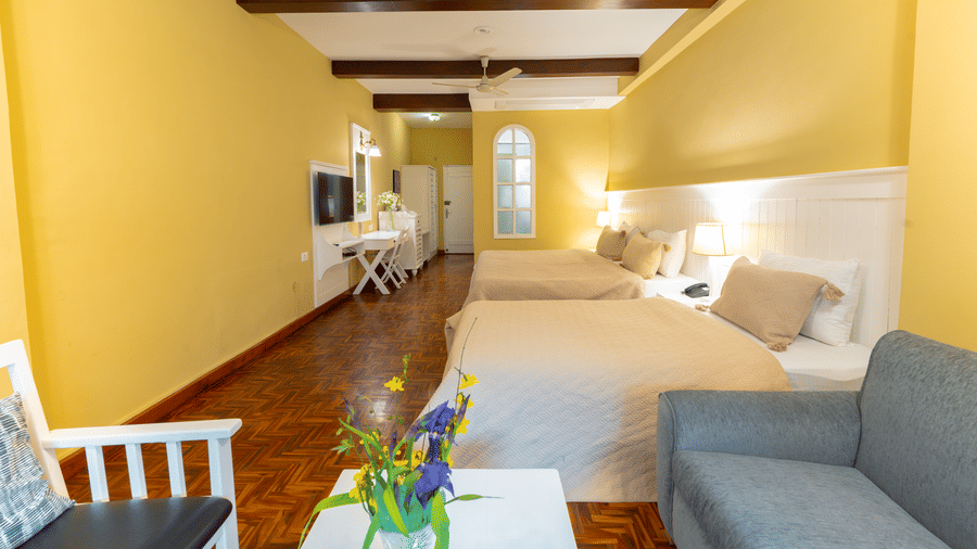 A wide-angle shot of a guest room with yellow walls, dark wood accents, and a grey sofa seating area - Johnson Lodge & Spa, Manali