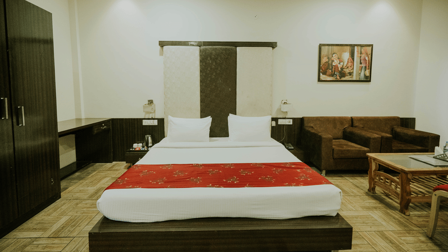 A bedroom at TGI Jahaj Mahal, Mandu featuring a king size bed with a red runner, a wardrobe, and a sofa.