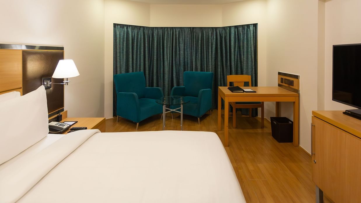 Superior Panoramic Rooms at The Residency Chennai featuring a plush bed with fresh linen facing the TV on a counter beside which is a work desk and a sitting space by the window