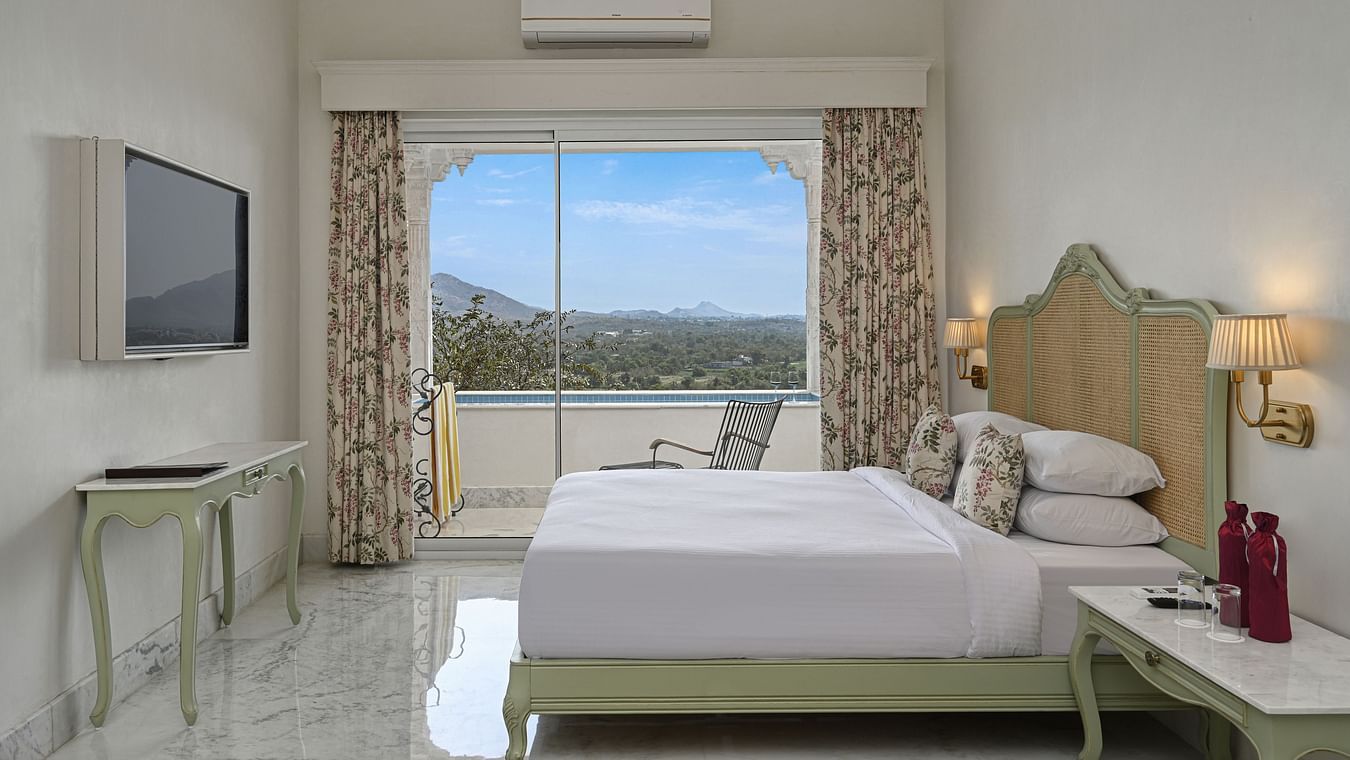 Side view of a  well-lit Plunge Pool Suite at Khas Mahal by Fateh Collection, Udaipur featuring a bed, seating area, and a large window with a view.