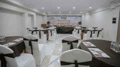 A well-lit banquet hall with elegant seating, white chair covers, and neatly arranged dining tables - Biznotel By Pride Surat