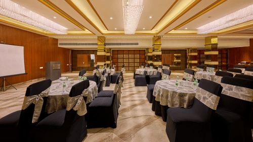 An image of a hall with blue chairs, round tables and a wall-mounted projector screen
