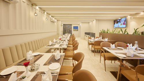 A restaurant dining room at Tulip Inn Gurugram with long rows of set tables, chairs, and a linear light-panelled ceiling.